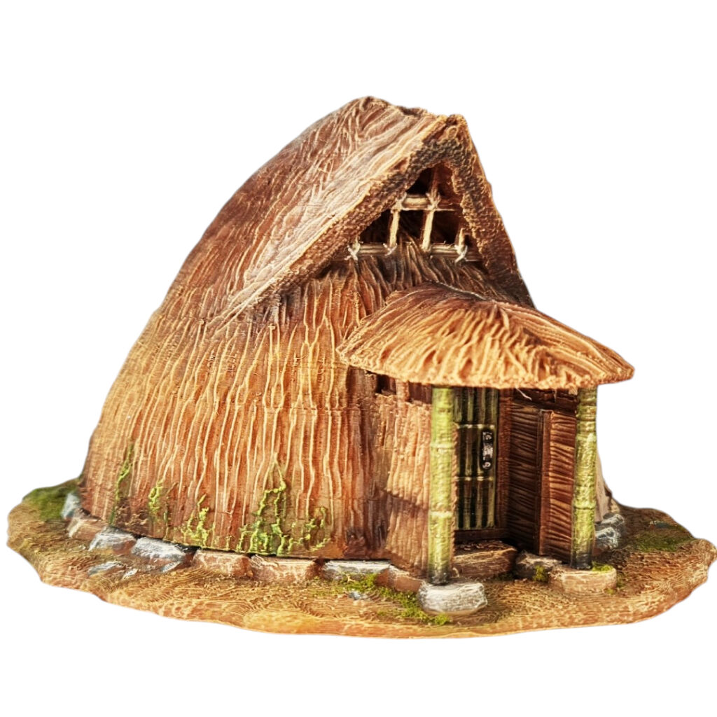 A 28mm scale 3D printed model of a Koyane-Minka, a small, circular Japanese folk house. The model features a rounded, bell-shaped thatched roof that curves toward the ground, a small sheltered entrance supported by two timber pillars, and a stone-lined foundation. The design reflects a primitive, organic mountain hermitage or rural storage hut.