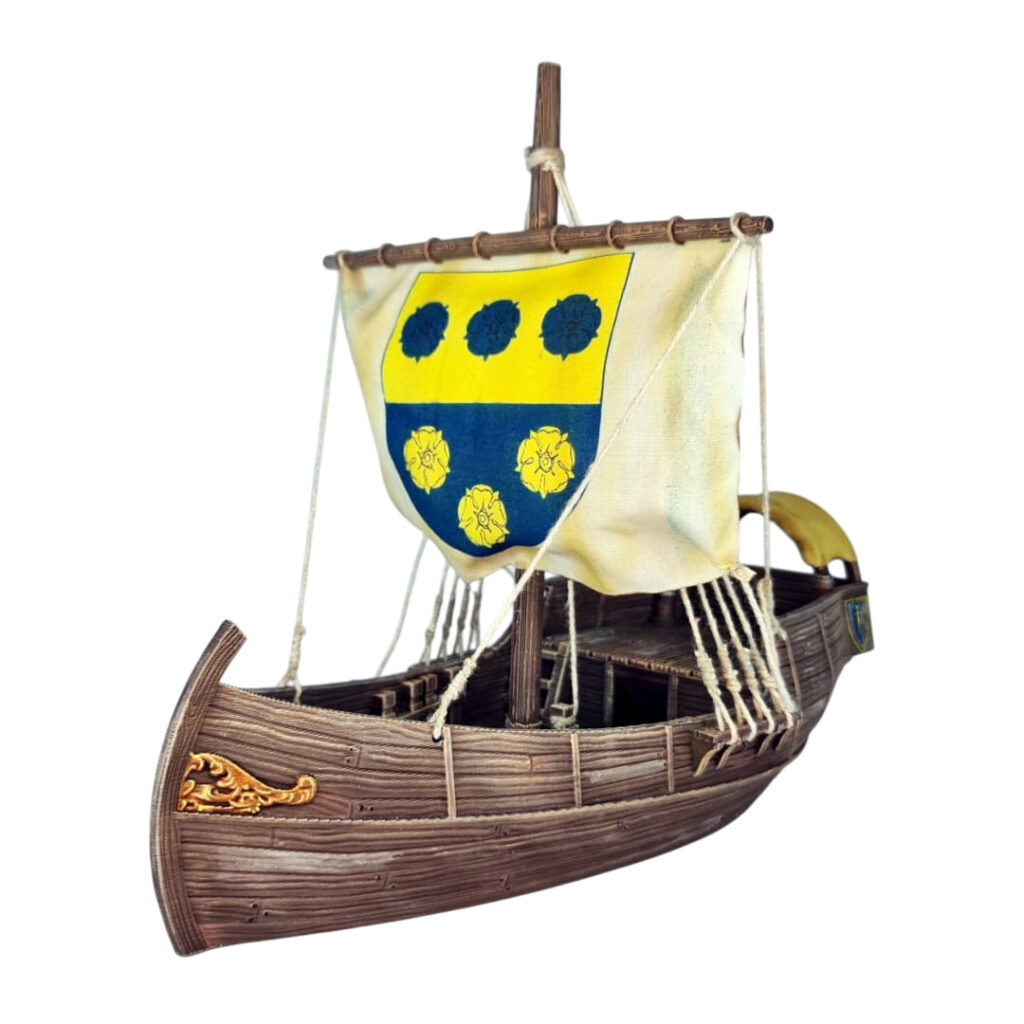 3D printed and painted model of a medieval merchant cog ship, front view. The ship has a detailed wooden hull, a single mast, and a square sail with a blue and yellow coat of arms.
