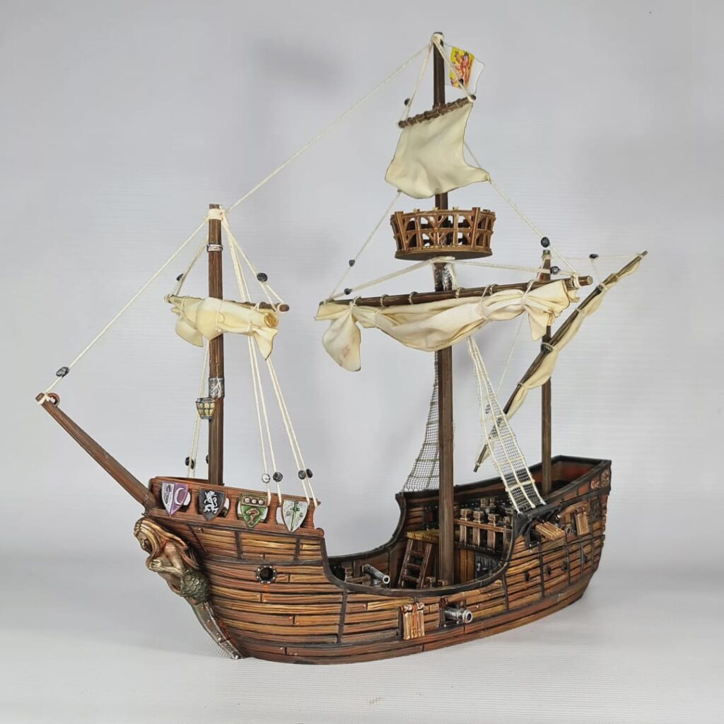 A fully painted 3D printed model of a 15th-century Caravel ship on a white background. The model features detailed wood textures, cannons, a mermaid figurehead, heraldic shields, masts with furled sails, and intricate rigging.