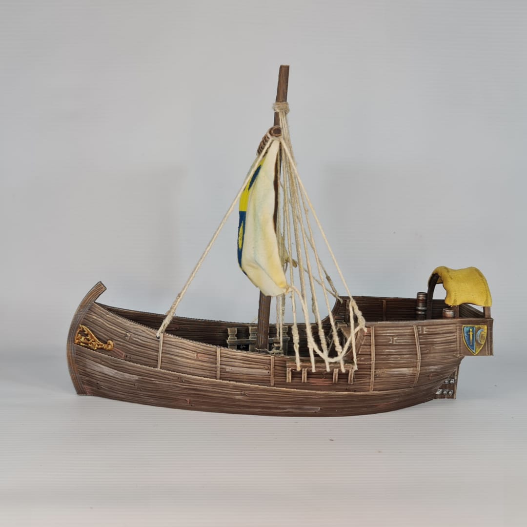 3D printed and painted model of a medieval merchant cog ship, front view. The ship has a detailed wooden hull, a single mast, and a square sail with a blue and yellow coat of arms.