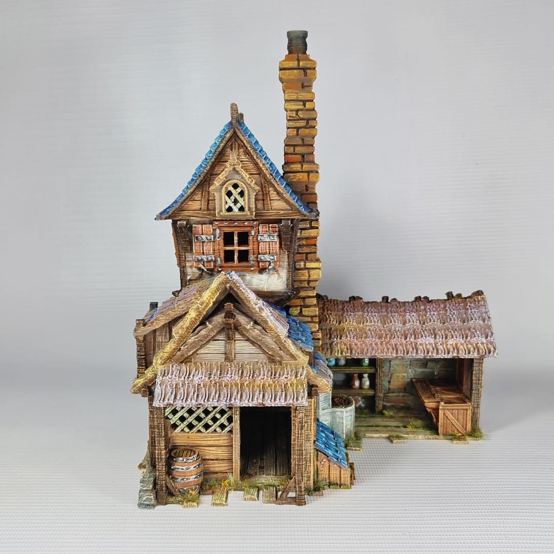 3D printed and painted miniature of a medieval blacksmith building with a stone foundation, wooden wattle-and-daub walls, a side waterwheel, thatched awnings, and a striking blue tiled roof.